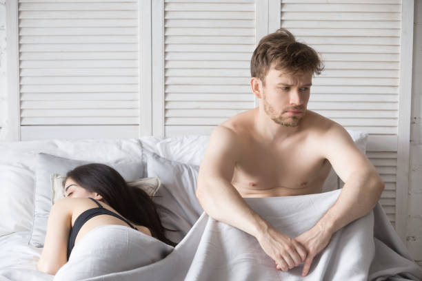 sfrustrowany mężczyzna i śpiąca kobieta leżąca w łóżku - men women contemplation sleeping zdjęcia i obrazy z banku zdjęć