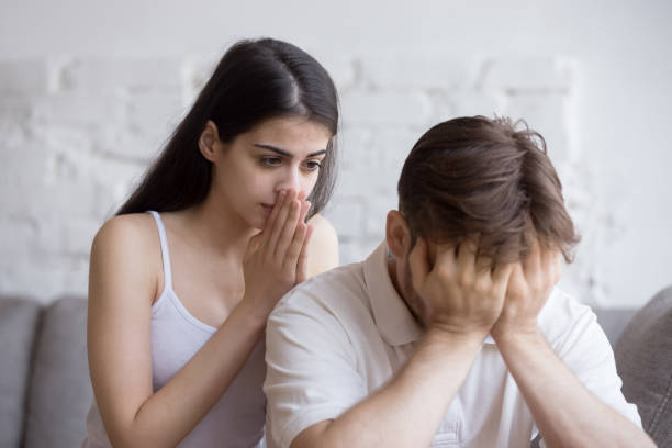 Unhappy young man and woman in quarrel sitting on couch Couple sitting on couch after quarrel. Unhappy man cover face with hands woman empathizes, feels guilty. Relation problems break up, difficulties or friend support after disagreement with a loved one woman comforting depressed friend stock pictures, royalty-free photos & images