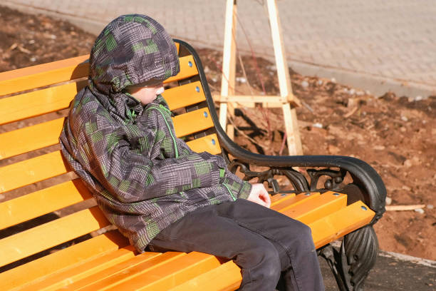 istock Boy sits on a bench in the Park and scratches the bench with a stone. 1057128906