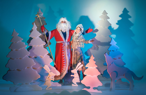 Russian Father Frost and Snow Maiden (Snegurochka) are standing together in a winter fairy forest. They are greeting and congratulating with Merry Christmas