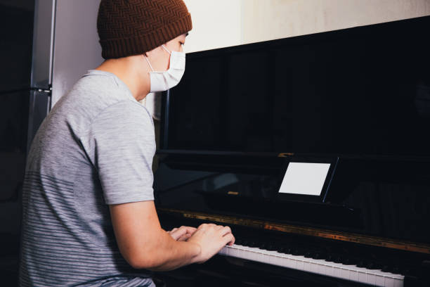 istock Young Asian male patient with sickness playing piano while using an empty copy space tablet screen at home 1057154802
