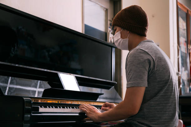 istock Young Asian male patient with sickness playing piano while using an empty copy space tablet screen at home 1057154868