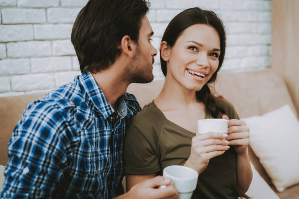istock Man Talking Smiling Woman with Cup on Brown Sofa. 1057157002