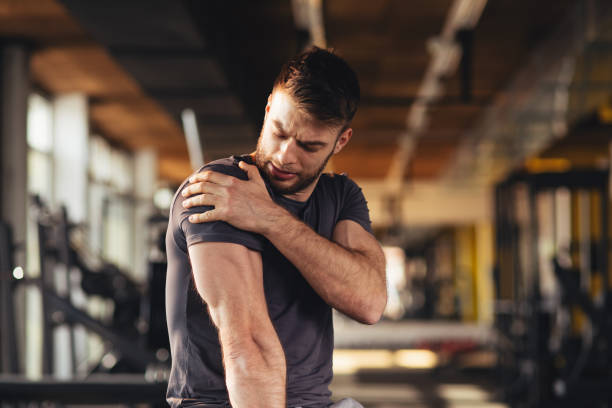 atractivo joven, sintiendo el dolor en el hombro en el gimnasio - pain fotografías e imágenes de stock