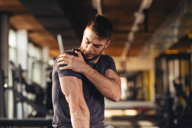 Handsome young man feeling the pain in shoulder at the gym stock photo