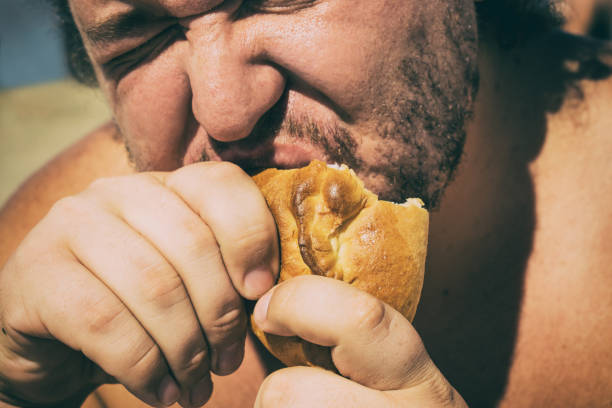 Fat man on the beach eating a pie. Overweight and unhealthy diet