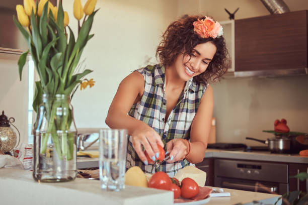 urocza kręcona latynoska dziewczyna gotuje w swojej kuchni. - stereotypical housewife women domestic kitchen brown hair zdjęcia i obrazy z banku zdjęć