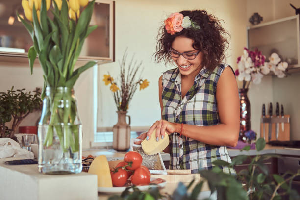 urocza kręcona latynoska dziewczyna gotuje w swojej kuchni. - stereotypical housewife women domestic kitchen brown hair zdjęcia i obrazy z banku zdjęć