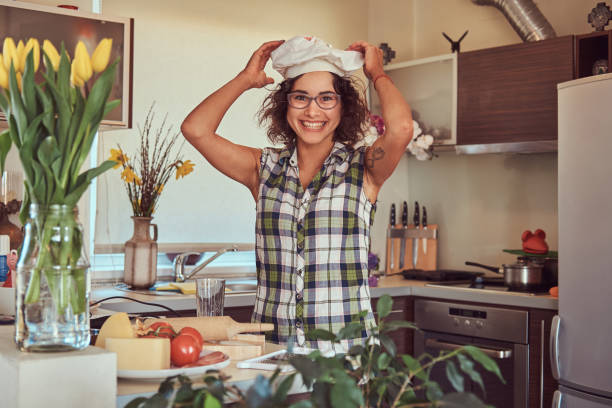 urocza kręcona latynoska dziewczyna gotuje w swojej kuchni. - stereotypical housewife women domestic kitchen brown hair zdjęcia i obrazy z banku zdjęć