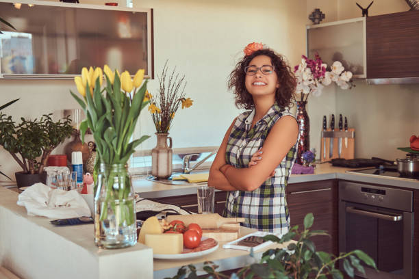 urocza kręcona latynoska dziewczyna gotuje w swojej kuchni. - stereotypical housewife women domestic kitchen brown hair zdjęcia i obrazy z banku zdjęć