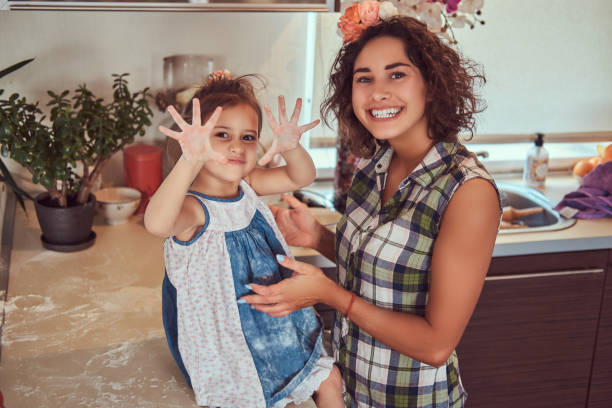 piękna hiszpańska matka i jej urocza córeczka bawią się w kuchni. - stereotypical housewife little girls family domestic kitchen zdjęcia i obrazy z banku zdjęć
