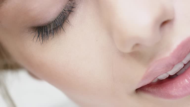 Dolly shot of female touching her skin. Beautiful woman is with closed eyes and pink glossy lips. She is against white background.
