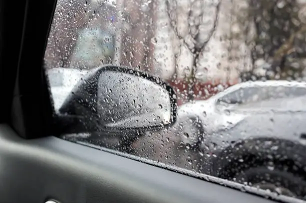 Raindrops on side rearview mirror in rainy day.