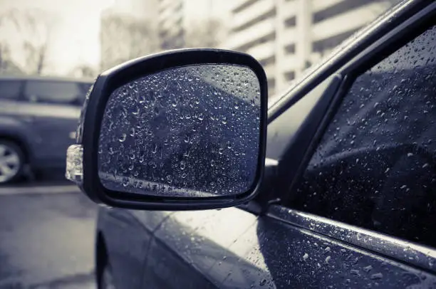 Raindrops on side rearview mirror in rainy day.