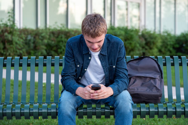 istock Happy male teenager texting while sitting on a bench. 1057189856