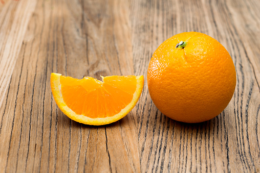 Whole orange and slice on wooden table.
