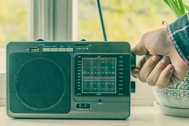 Photo of hand adjusting the settings of vintage old radio, search for radio station wave f