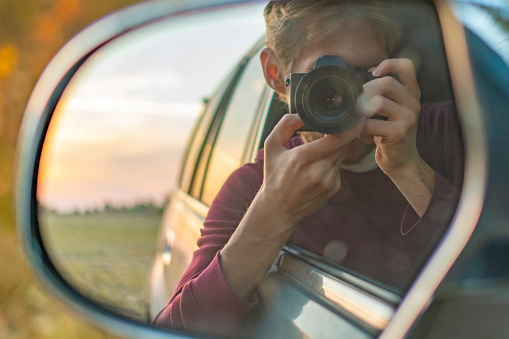 young driver taking a self portrait with professional camera in the car window
