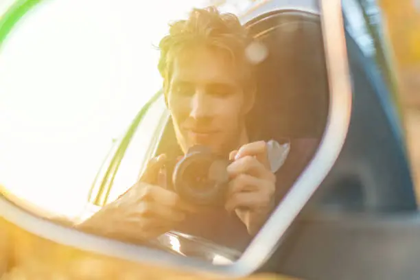 Photo of young driver taking a self portrait with professional camera in the car window  f