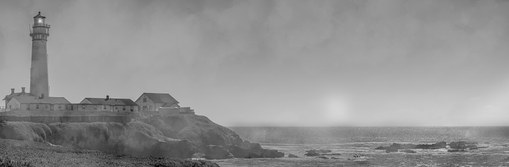 Fog rolls in on Pigeon Point Lighthouse with the sun still up on the California coastline