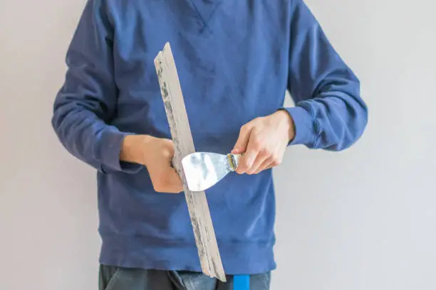 close up man holding putty knifes plastering the wall, working and repair home