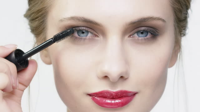Woman applying mascara against white background