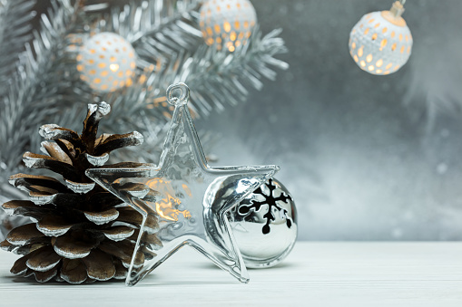 decorative glass star, silver cone and christmas jingle bells on blurred grey background with fir tree branch and garlands