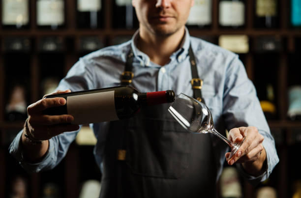 Male sommelier pouring red wine into long-stemmed wineglasses. Male sommelier pouring red wine into long-stemmed wineglasses. Waiter with bottle of alcohol beverage. Bartender at bar counter pour elite drink into long-stemmed glass sommelier photos stock pictures, royalty-free photos & images