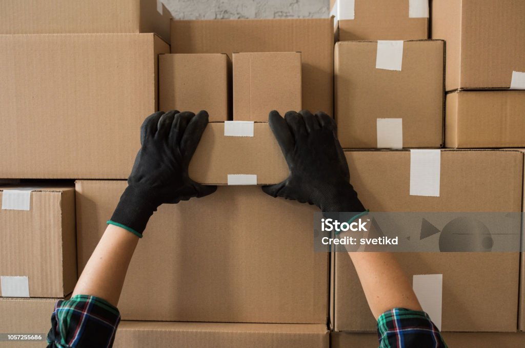 Cardboard boxes ready for delivery Cardboard boxes stocked by the wall in warehouse. Ready for delivery. Delivery person picking one of boxes. Warehouse Stock Photo