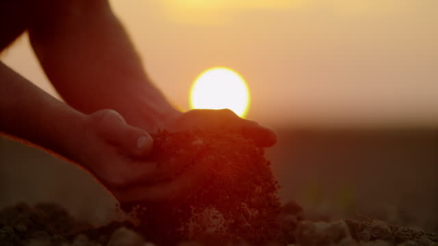 SLO MO Farmer's hands scooping dirt on a field at sunset