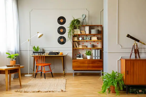 Photo of Vinyl records decorations on a gray wall with molding and wooden furniture in a retro home office interior for a writer. Real photo.