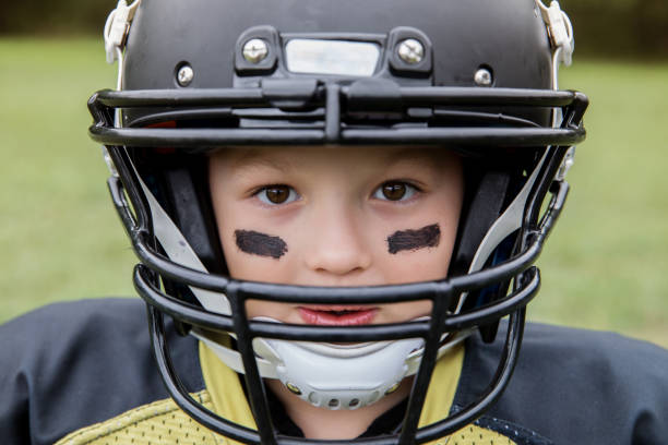 muchacho es poco jugador de fútbol americano liga mirando a cámara a través del casco - youth league american football childhood helmet fotografías e imágenes de stock