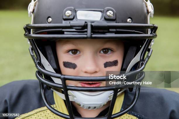 Photo libre de droit de Garçon Est Petit Joueur De Football Américain Regarder Dans La Caméra À Travers Casque banque d'images et plus d'images libres de droit de Football américain