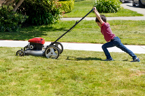 Stock photo of a small boy attempting to mow a lawn in a suburban neighborhood .