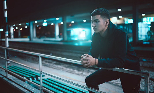 Young teenage handsome man waiting on train station alone.