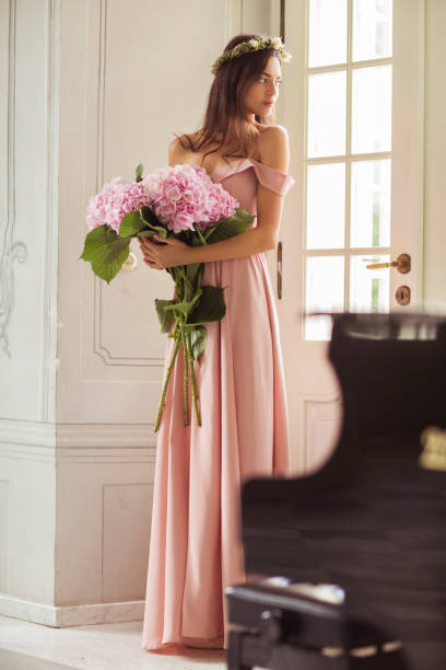 Beautiful Woman with hydrangeas in arms standing in nice palace's interior. Woman in long beautiful dress. pink gown stock pictures, royalty-free photos & images