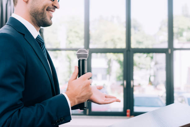 istock cropped image of smiling speaker gesturing and talking into microphone at podium tribune during seminar in conference hall 1057329916