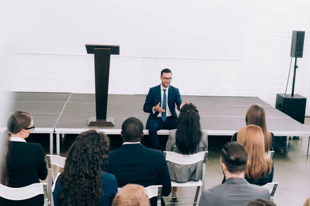 istock high angle view speaker sitting on stage during seminar in conference hall and talking to multicultural audience 1057330096