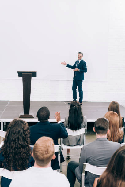 istock smiling lecturer talking to multicultural audience during seminar and pointing on screen in conference hall 1057330106