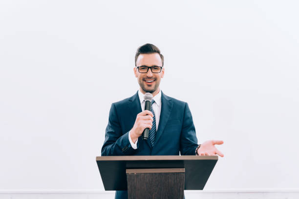 istock smiling speaker gesturing and talking into microphone at podium tribune during seminar in conference hall 1057330138
