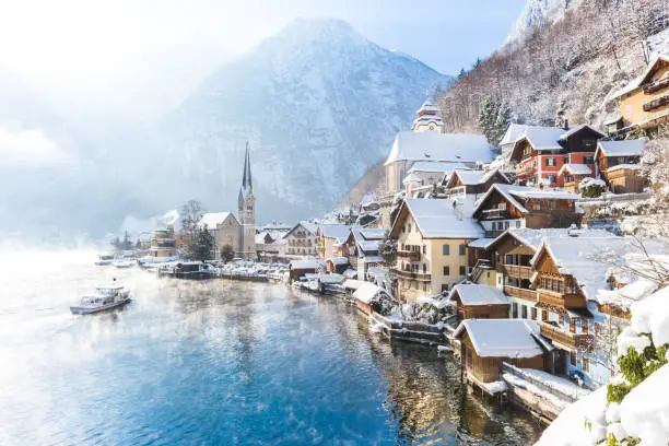 Classic postcard view of famous Hallstatt lakeside town in the Alps with passenger ship on a beautiful cold sunny day with blue sky and clouds in winter, Salzkammergut region, Austria