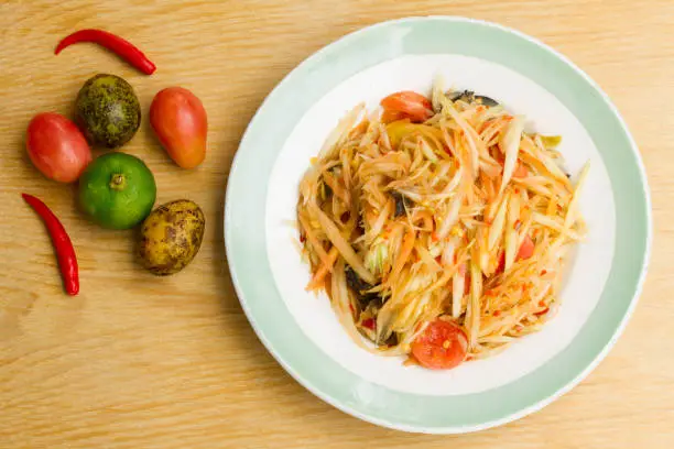 Photo of Papaya salad in a white plate on a wooden table , Space for text input