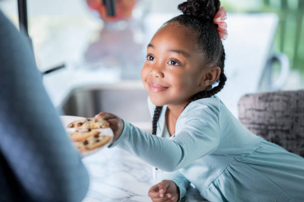 istock Adorable elementary age little girl eating cookies in kitchen 1057343936