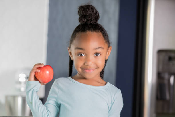istock Smiling elementary age girl holding an apple in kitchen. 1057343942