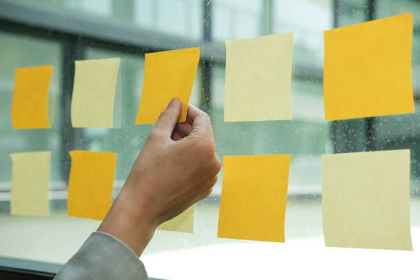 istock hand hold adhesive notes on glass wall. Sticky note paper reminder schedule for creative idea & business brainstorming 1057359104