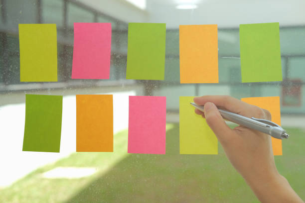 istock hand write on adhesive notes on glass wall. Sticky note paper reminder schedule for discussing creative idea & business brainstorming 1057359866