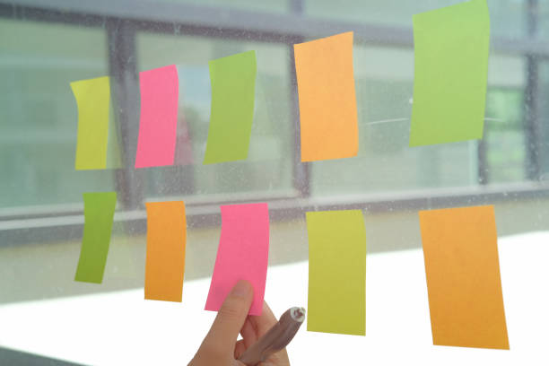 istock hand hold adhesive notes on glass wall. Sticky note paper reminder schedule for creative idea & business brainstorming 1057359870