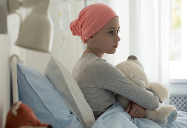 Sick child with cancer sitting in hospital bed holding teddy bear Sick child with cancer sitting in hospital bed holding teddy bear hospice photos stock pictures, royalty-free photos & images