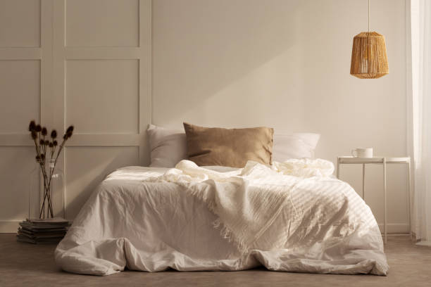 istock Pillows on white bed between flowers and table in minimal bedroom interior with lamp. Real photo 1057384660