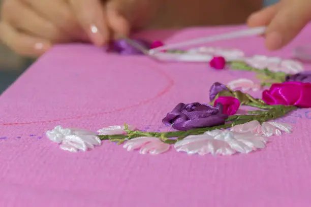 a woman is doing ribbon embroidery on pink fabric